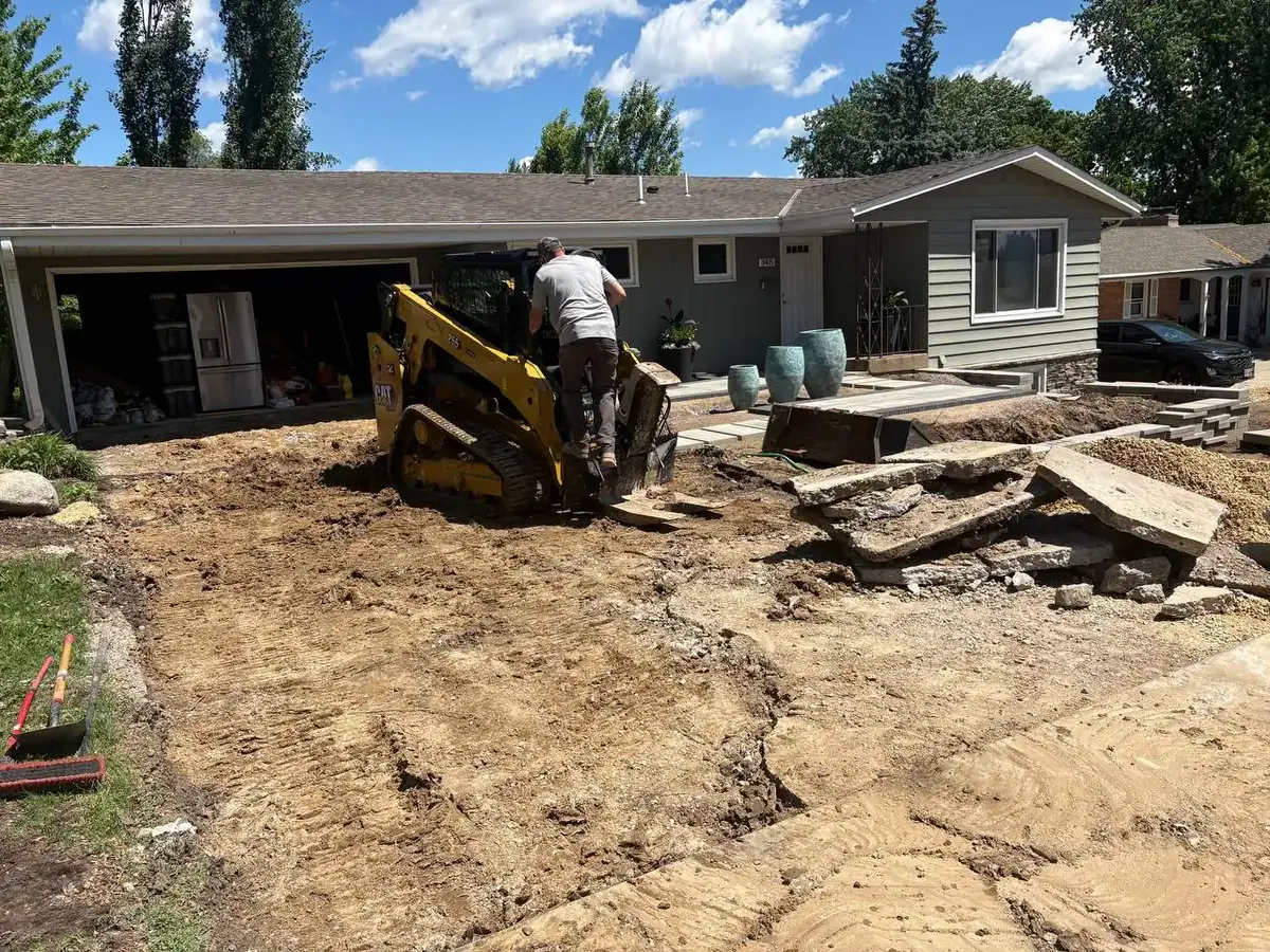 A skid steer tearing out an old concrete driveway in front of a house